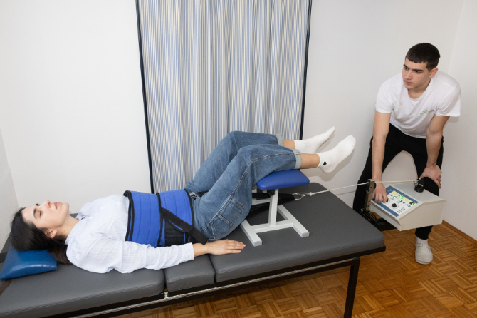 Pacijentkinja leži na trakcionom stolu dok fizioterapeut podešava aparat za trakciju kičme u Fizio Ahil centru Beograd